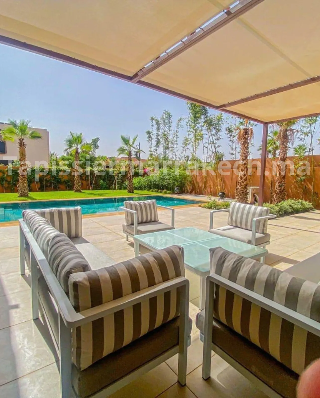 Salon de jardin avec canapés et fauteuils en tissu rayé près d'une piscine à Marrakech