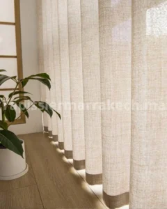 Voilages beiges devant une fenêtre avec une plante sur le côté